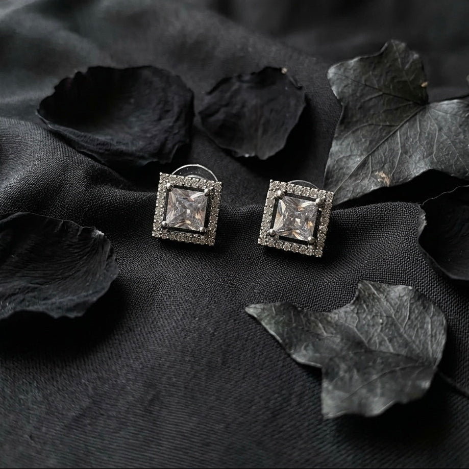 Square stud earrings with clear gemstones on black fabric with leaves
