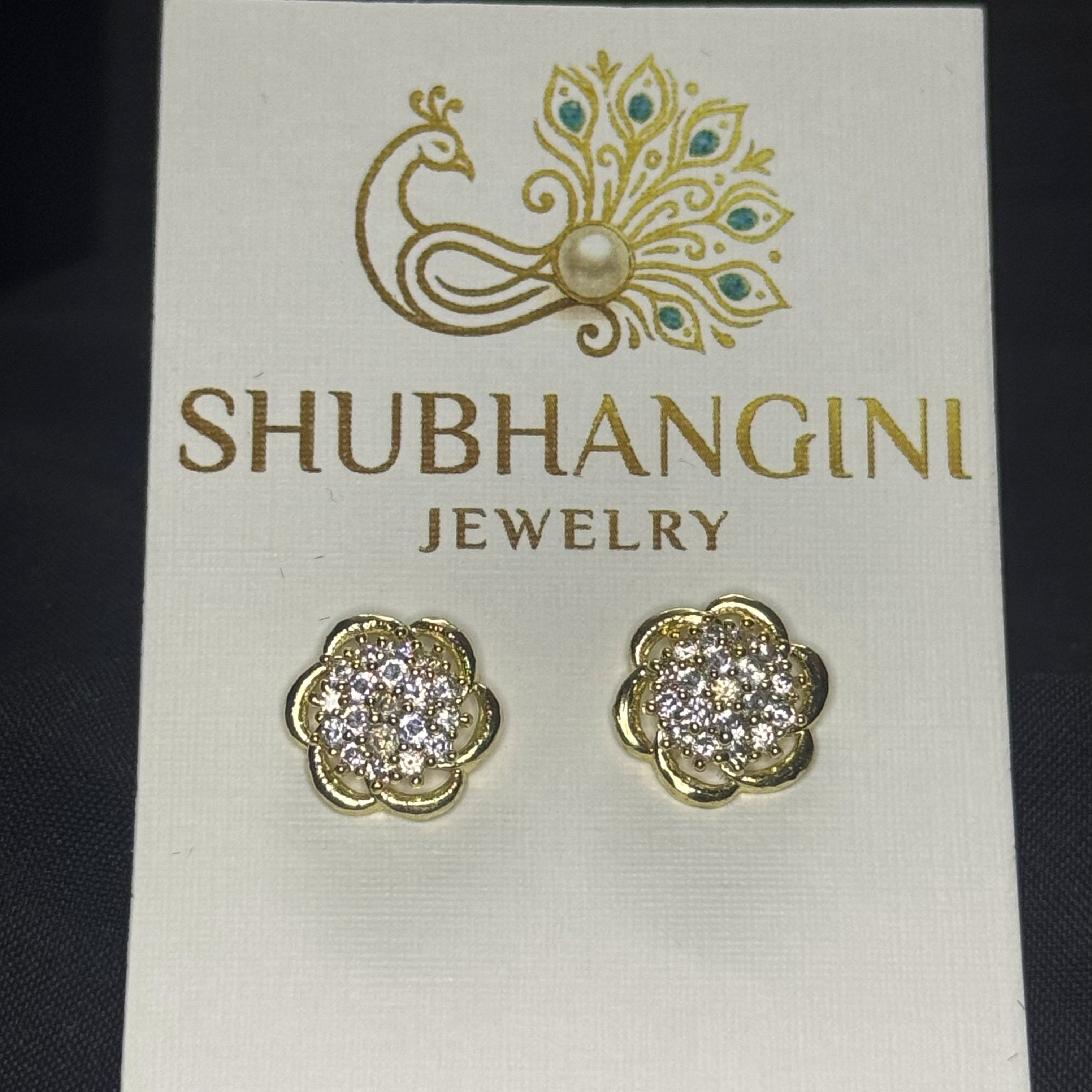 Gold and diamond earrings on a Shubhangini Jewelry card against a black background