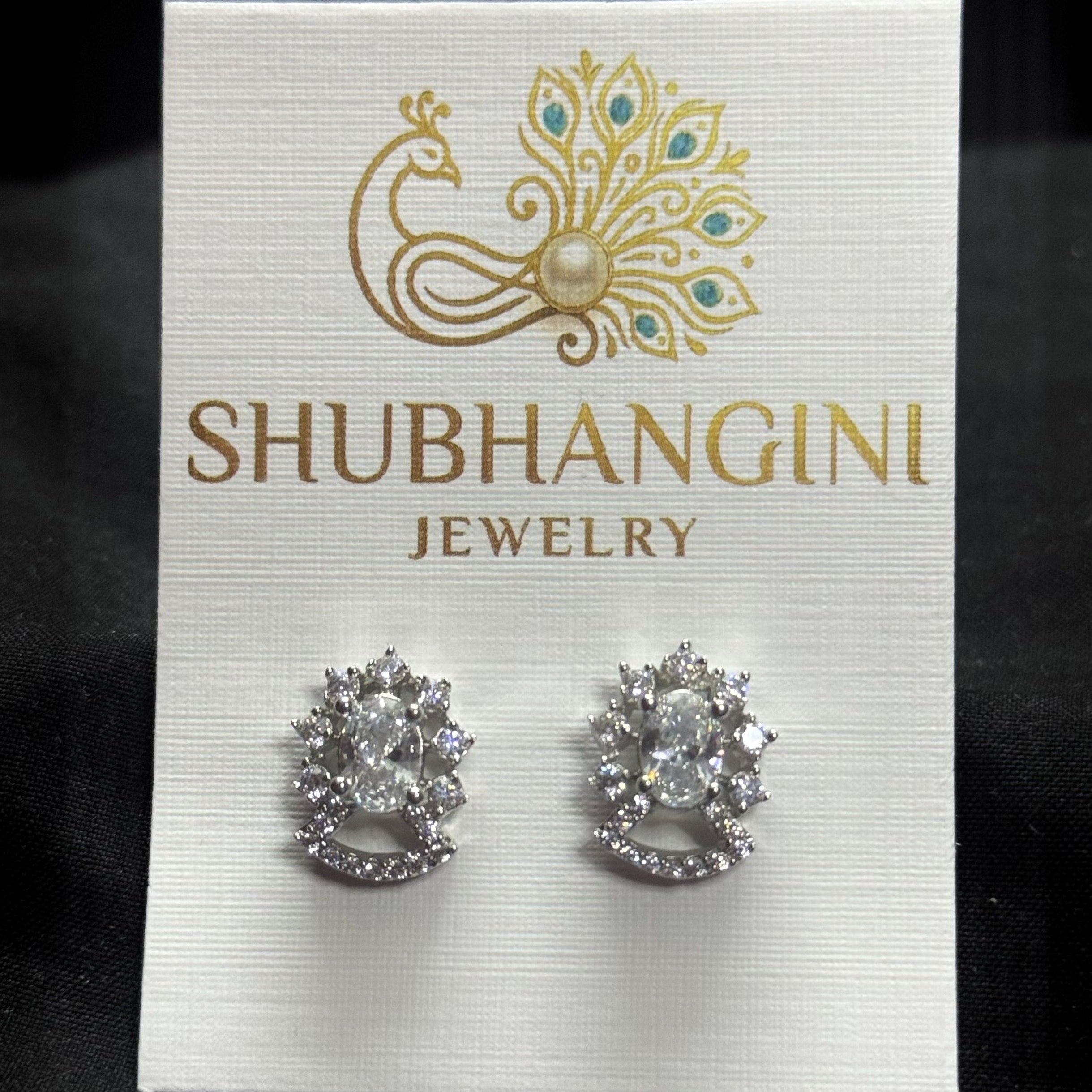 Pair of silver earrings on a Shubhangini Jewelry card against a black background