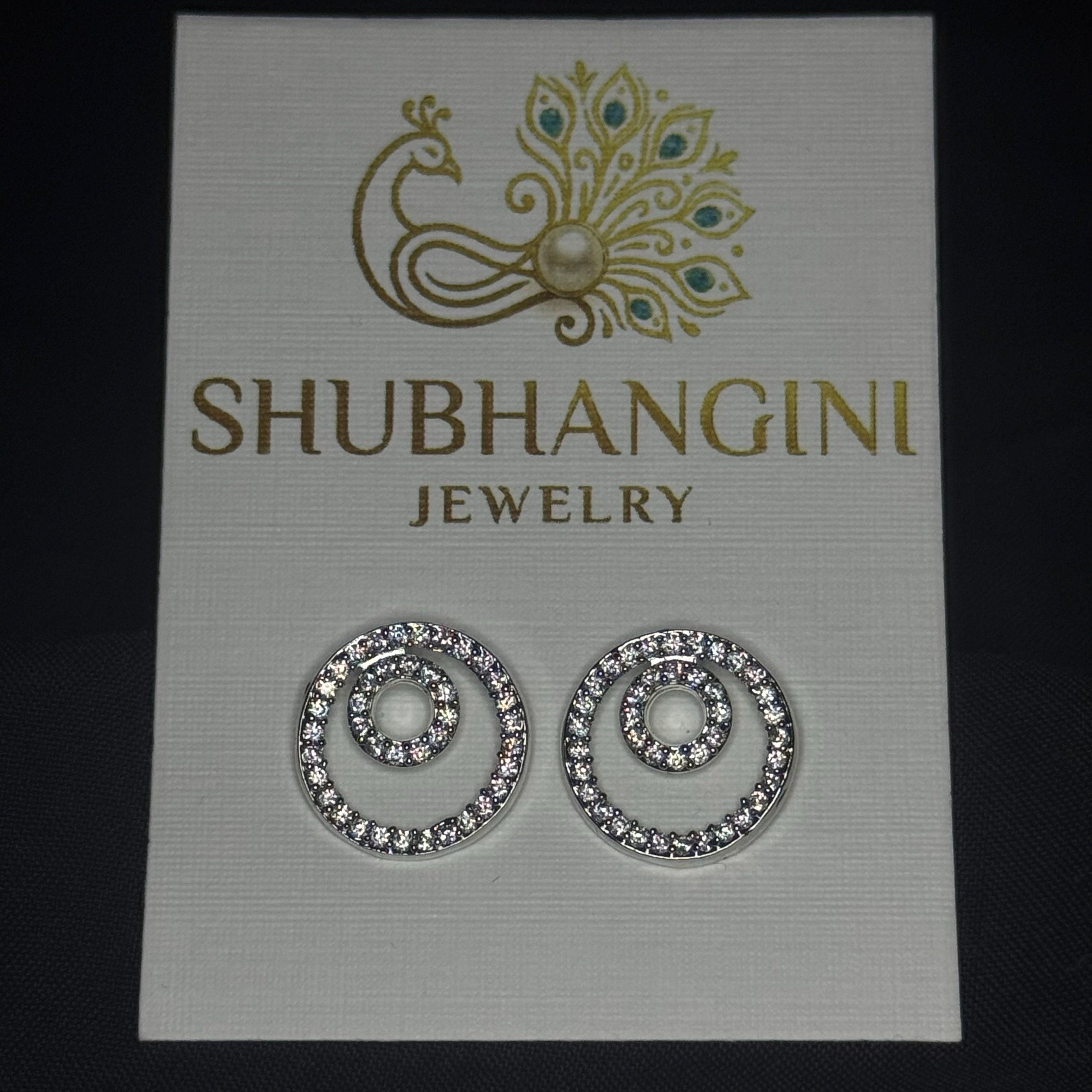 Shubhangini jewelry card with a pair of earrings on a dark background