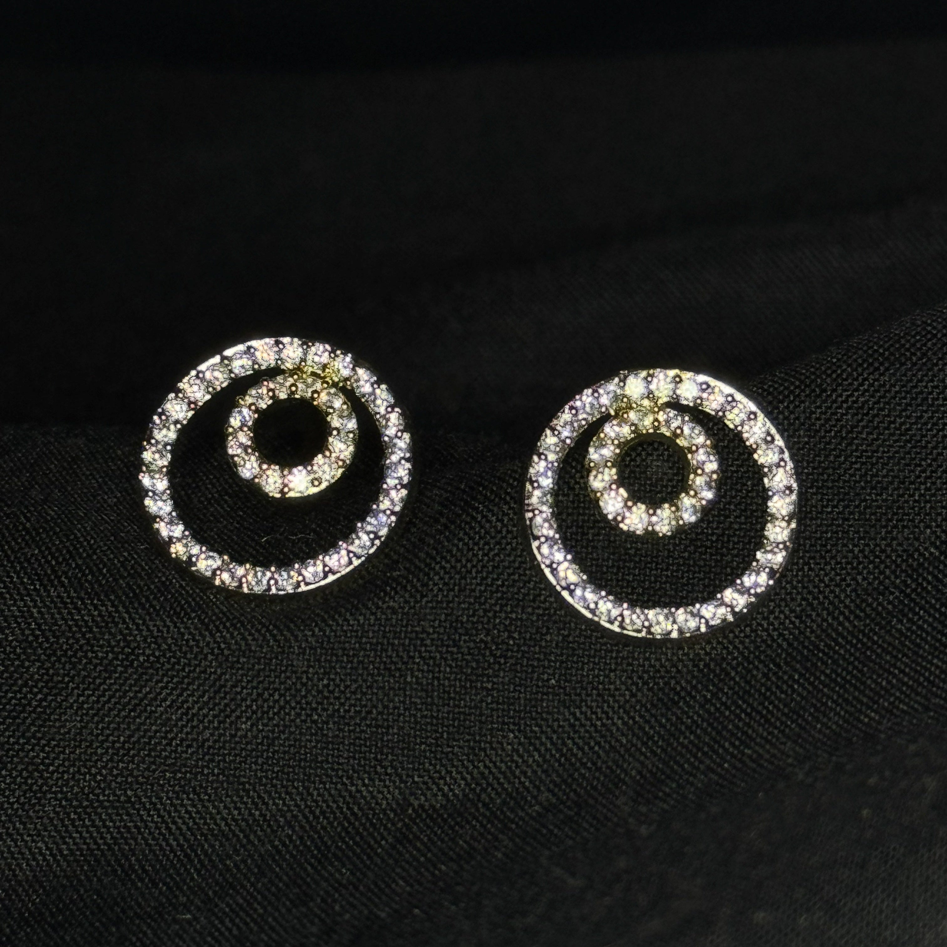 Pair of spiral-shaped earrings with rhinestones on a black fabric background