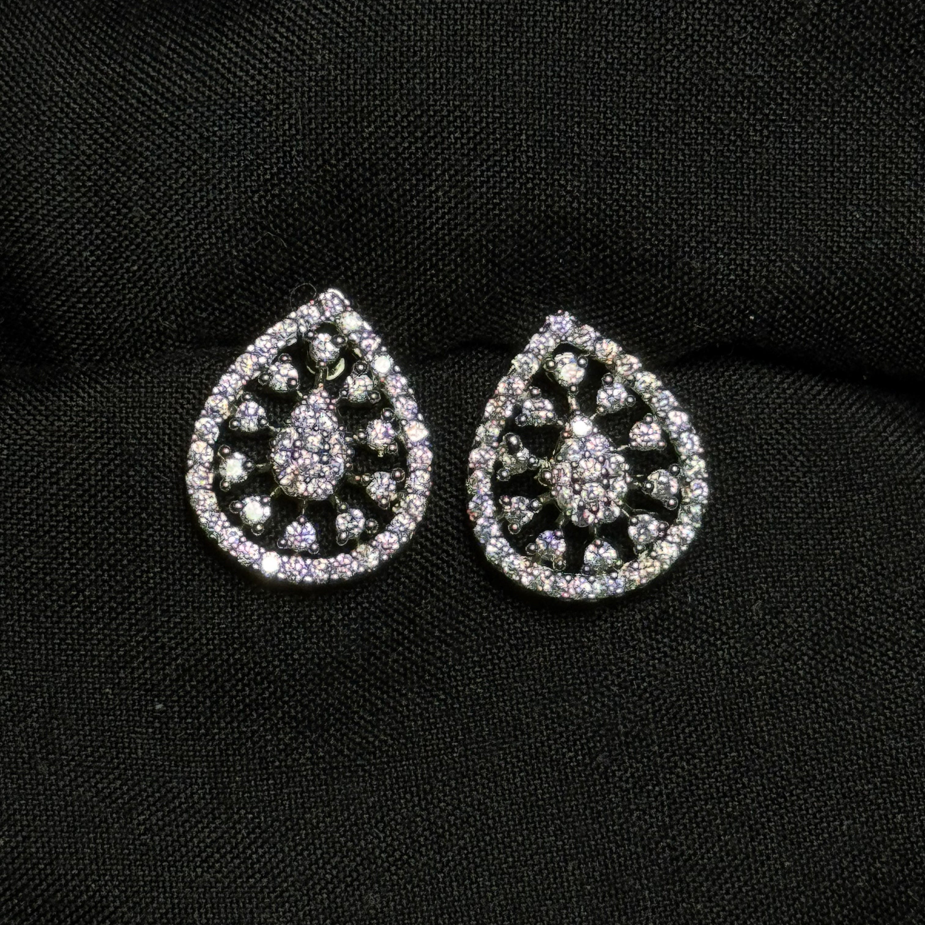Teardrop-shaped silver earrings with gemstones on a black background