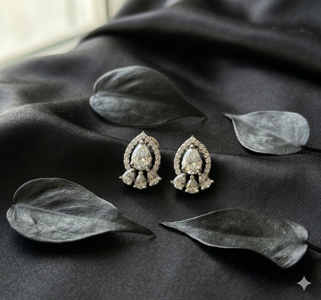 Pair of diamond earrings on a dark fabric surface with leaves
