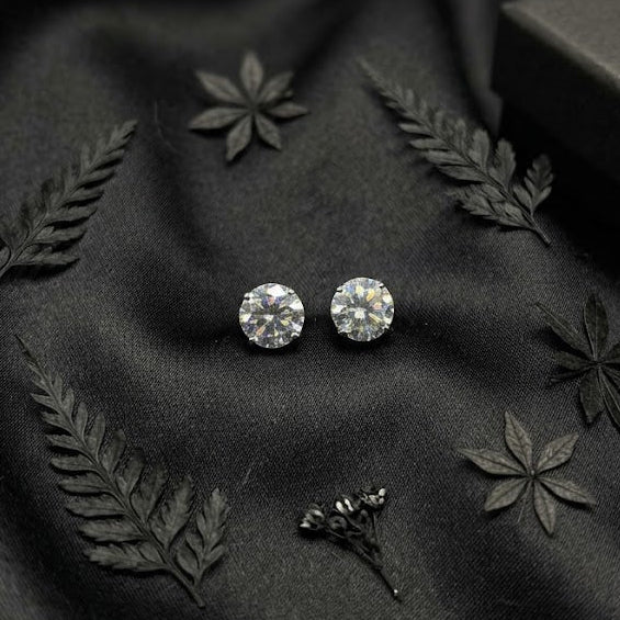 Pair of silver stud earrings on black fabric with decorative leaves.