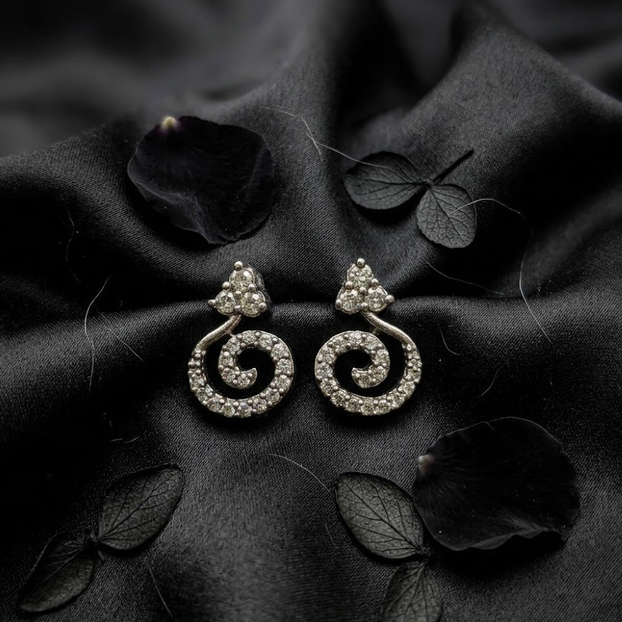 Pair of silver spiral earrings on a dark fabric background with leaves.