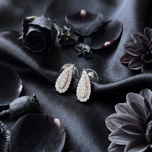 Pair of silver earrings on a dark fabric background with flowers and leaves.